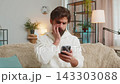 Upset displeased Indian man guy using smartphone reading bad news sitting on couch in living room 143303088
