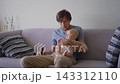 Father holding baby son while drinking beer on couch. Concept of alcohol use, family life, and parental responsibility. 143312110