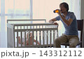 Father sitting beside baby in crib, drinking beer and talking to his son. Concept of alcohol use and parental responsibility 143312112
