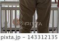 Father helping five-month-old son turn onto his belly in crib beside baby monitor camera. Infant care 143312135