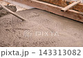 Fresh wet concrete spreads inside wooden formwork while diagonal screed tool levels surface at construction site, with rough slurry texture, damp sheen, weathered timber, and warm natural light. 143313082