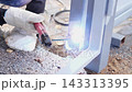 Close-up outdoor repair scene shows welding contact on gray metal post, glowing seam, heat marks, and tiny sparks over rough gravel, with welding, welder, glove, hand detail, showing holder 143313395