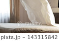 In a bright bedroom, a steward lifts a sheet up with his hands and spreads it onto the surface of the double bed mattress. Slow motion. Close up shot 143315842