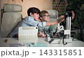 In the foreground of the shot, a 3D printer is printing a part, while at the same time, a older boy explains to his friend in glasses how the printer works. Slow motion. Medium close-up shot 143315851