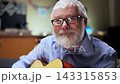 At home, in a brightly lit living room, a grey haired man with glasses sits on a sofa with a guitar and chats with someone off camera. Camera movement directly towards the man. Slow motion shot. Big 143315853