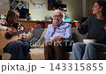 In the living room, an elderly man sits on the couch, completely emotionless, withdrawn, and lost in thought, indifferently eating popcorn. He is surrounded by his granddaughters, who are 143315855