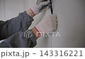 Close-up of electrician placing socket box into wall hole and laying cable in groove. Detailed install process in apartment. 143316221