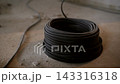 Rolled electrical cable prepared for installation in apartment under renovation. Worker on ladder in background during electrical setup. 143316318