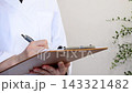 A person in a white coat writing on a document on a clipboard. 143321482