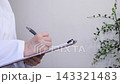 A person in a white coat writing on a document on a clipboard. 143321483