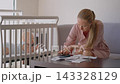 Worried mother reviewing household bills beside baby in crib. Financial stress of motherhood. 143328129