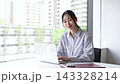 一位三十多歲的日本女性一邊使用筆記型電腦一邊微笑。 143328214