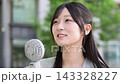 一位微笑的20多歲日本女性正在用便攜式風扇為自己降溫。 143328227