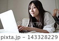 一位二十多歲的日本女性在床上操作筆記型電腦時面帶微笑。 143328229