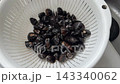 A colander full of clams being washed under running water 143340062