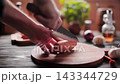 Hand with Knife Cutting Sweet Potato on Round Wooden Board 143344729