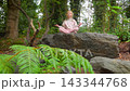 Girl Sits on Stone in Lotus Pose in Park Sunny Day Meditates Smiles 143344768