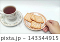 Hand taking crispy cracker from plate near hot black coffee cup 143344915