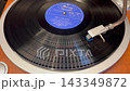 A rotating black analog record and the tonearm of the turntable. 143349872