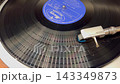 A rotating black analog record and the tonearm of the turntable. 143349873