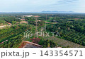 Aerial view of lush green fields. Electric towers stand tall across the landscape. Mountains loom far in the distance 143354571
