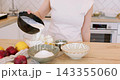 Homemade recipe. Pastry cooking. Female chef pouring liquid cream in glass bowl with cottage cheese eggs on table with fresh fruit. 143355060