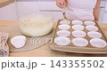 Preparing muffin. Treat recipe. Woman chef hand pouring batter from glass bowl spoon in paper liners in baking tin on home kitchen counter. 143355502