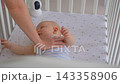 Mother stroking five-month-old baby in crib and placing baby monitor camera inside. Infant care 143358906