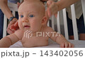 Close-up of five-month-old baby boy in crib being gently stroked by parents and older brother. Loving family moment. 143402056