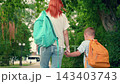 Mom smiling young son walking together outdoors. Mom young school child son walking to school, he carrying backpack, holding mother hand. Child rearing concept. Happy family walk in park. Education 143403743