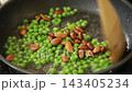 Stirring green peas and almonds in a frying pan 143405234