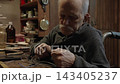 Elderly craftsman working in his old workshop, carefully restoring collectible Japanese bladed weapons 143405237