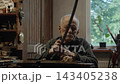 Elderly craftsman working in his old workshop, carefully restoring collectible Japanese bladed weapons 143405238
