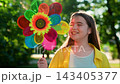 Little girl smiling on lawn summer park, holding pinwheel toy in hands. Happy child plays with pinwheel toy, green park. Child childhood. Family picnic in outdoors. Child in nature. Holiday teen girl 143405377