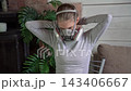 Woman putting on protective respirator mask with dual filters in living room, medium close frontal view, securing head straps in calm focused motion, soft natural side light, casual interior scene 143406667