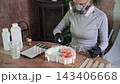 Woman wearing respirator and gloves pouring clear liquid from spray bottle into heart-shaped silicone mold with pink resin roses on wooden table, focused studio craft scene 143406668
