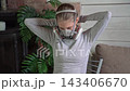 Young woman adjusting protective respirator mask while seated in home workshop, soft natural side light, focused preparation for painting or DIY project 143406670