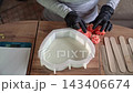 Gloved hands arranging pink soap roses beside heart-shaped silicone mold filled with pale liquid on wooden table, overhead craft workspace, soft natural light 143406674