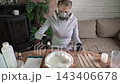 Woman in respirator and gloves mixing resin in heart-shaped mold on wooden table in cozy home workshop with daylight lighting and craft supplies visible across tabletop 143406678