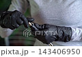 Close-up of gloved hands inserting metal drill bit into handheld rotary tool showing precise assembly motion and protective nitrile gloves in soft natural light 143406950