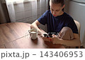 Young woman scrolling phone at wooden kitchen table beside ceramic coffee mug in soft window light relaxed morning indoor lifestyle moment thoughtful concentration 143406953