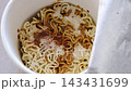 Description: Close up shot of hot water being poured from a kettle into an open instant noodle paper box container with flavor seasoning packets, perfect for quick meals, fast food, convenience food  143431699