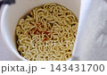 Description: Close up shot of hot water being poured from a kettle into an open instant noodle paper box container with flavor seasoning packets, perfect for quick meals, fast food, convenience food  143431700