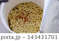 Description: Close up shot of hot water being poured from a kettle into an open instant noodle paper box container with flavor seasoning packets, perfect for quick meals, fast food, convenience food  143431701
