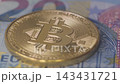 Close up shot of a shiny physical gold Bitcoin coin lying on Euro banknotes, representing cryptocurrency investment, digital assets, cash currency exchange, and modern financial concepts. 143431721