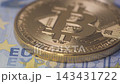 Close up shot of a shiny physical gold Bitcoin coin lying on Euro banknotes, representing cryptocurrency investment, digital assets, cash currency exchange, and modern financial concepts. 143431722