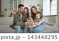 Happy family talk on video call with friends family. Mother father two children holding smartphone talking speaking online. Family mom dad parents baby girls kids smiling laughing enjoying moment 143448295