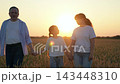 Dad mom child daughter smiling walking hand in hand wheat field, sunset. Happy farming family with child walk through wheat field. Farmer parents, little daughter enjoying nature together, countryside 143448310