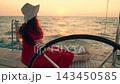 Lady in red dress white hat enjoys ocean sunset on deck of yacht. Ship sails on sea, woman travels on ship. Girl relaxes ocean vessel rocks on waves. Sea voyage. Dream trip, vacation sun sky water 143450585