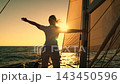 Lady captain travels ocean yacht watching waves sunset. Young woman sailing yacht under white sail raising her arms, dreaming flying over ocean. Ship sails sea woman looks sun. Girl in travels ocean 143450596